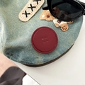 Detail of blue denim phone grip with leather patch, bear embroidery, and button texture - Burgundy