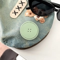 Close-up of light blue denim accessory with mint green faux leather button and embroidery - Green