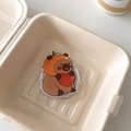 Detail shot of a cute brown bear acrylic phone grip with a red heart in a gift box - Magnetic Versatile Capybara No.3 (Orange Hoodie Style)