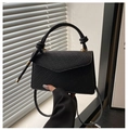 Detail view of black embossed leather handbag featuring knot handle and gold hardware - Black