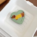Detail of heart-shaped leather phone grip featuring embroidered puppy and slogan - Green