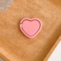 Close-up of a pink heart-shaped phone ring holder on a rustic wooden background - Pink