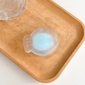 Detail view of a matte fish-shaped phone grip on a natural light wood tray - Blue