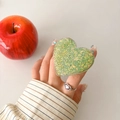 Close-up of a heart-shaped green glitter phone grip holder on a desk near a red apple - Light Green