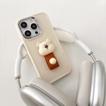 Detalle de funda crema con osito y correa de cuero marrón en un soporte para cascos - Funda Albaricoque Oso Blanco / iPhone 7/8/SE 2020