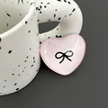 Macro detail of a pink heart-shaped phone grip featuring a black bow design - Pink
