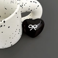 Macro shot of heart-shaped black phone grip with white bow pattern on textured ceramic cup - Black