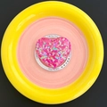 Macro shot of glitter-filled pink heart MagSafe phone grip in a colorful ceramic plate - Rose Red