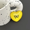 Macro shot of yellow heart phone grip with black bow print on white textured cup - Yellow