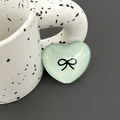 Close-up of heart-shaped light green phone grip with a black bow pattern on a ceramic mug - Light Green