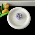 Purple cat paw shaped collapsible phone grip shown on a decorative white ceramic plate - Transparent Stand / Purple