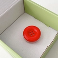 Close-up of a vibrant red button-shaped phone grip inside its mint green packaging box - Red