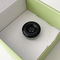 Detail of a black four-hole button phone socket grip in its green packaging box - Black