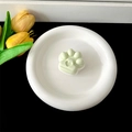 Detailed view of a cute light green cat paw phone grip placed on a white ceramic plate. - Transparent Stand / Light Green