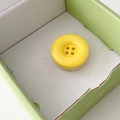 Macro shot of yellow button-shaped phone grip stand in a light green gift box - Yellow