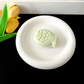 Close-up of light green fish-shaped phone grip on a white plate with floral accents - Transparent Stand - Two-tone Fish / Light Green