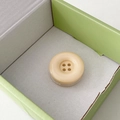 Close-up of a round cream-yellow four-hole resin button phone grip in a pastel box - Off-white
