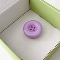 Detail view of a purple candy button phone grip with a cute 4-hole resin design in a box - Light Purple