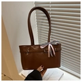 Detail of glossy brown patent leather shoulder bag with decorative bow and metal buckle - Tan