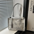 Silberne Tragetasche mit Schmetterlingsdruck und Quaste in minimalistischem Ambiente - Silber
