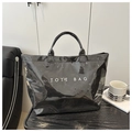 Close-up of a black glossy tote bag with white TOTE BAG text in a minimalist setting - Black