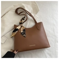 Detalle de bolso tote marrón con asa de pañuelo decorativo sobre fondo de tela blanca - Tostado