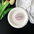 Detailopname van roze smiley spiegel telefoonhouder op wit keramisch schaaltje met tulp - Roze