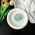 Close-up of a green smiley face mirror phone grip placed on a white ceramic tray - Light Green