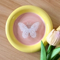 Draufsicht auf einen Keramikteller mit Schmetterling, gelbem Rand und rosa Mitte - Weiß