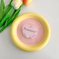 Draufsicht eines rosa Herz-MagSafe-Halters mit Romantic-Schriftzug auf gelbem Keramikteller - Rosa Romantic