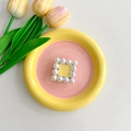 Detail of square gold metal phone grip with white faux pearl border on floral ceramic tray - Yellow