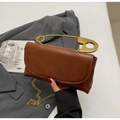 Detail of a brown leather bag featuring a large gold safety pin handle on a gray blazer - Brown