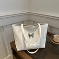 Elegante borsa tote bianca con trama marmorizzata e farfalla argentata su tavolo - Bianco