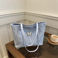 Pale blue textured tote bag with silver butterfly emblem and long shoulder straps - Blue