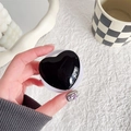 Primo piano di un supporto per telefono a cuore nero lucido tenuto in mano per scrivania - Supporto Magnetico-Cuore in Vetro di Cristallo-Nero