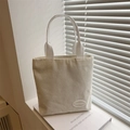 Bolso tote minimalista de pana beige sobre libros bajo una suave luz natural de ventana - Blanco
