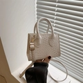 Mini borsa bianca a mano con trama a coccodrillo e fibbie dorate su uno scaffale - Bianco
