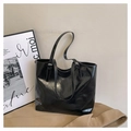 Detail of glossy black leather tote bag with side metal buckle on a beige backdrop - Black