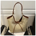 Detalle del bolso tote de paja trenzada con asas de cuero marrón y un lazo decorativo - Marrón