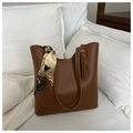 Dettaglio borsa tote in pelle marrone caramello con foulard in seta su divano bianco - Stile Caramello Opaco / Cuoio