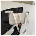 Detalle de bolso bandolera de cuero crema con cierre dorado sobre fondo de cama blanca - Blanco
