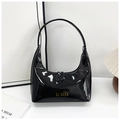 Detalle de bolso de hombro en charol negro brillante con logo dorado en entorno chic - Negro