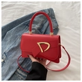 Primo piano di borsa in pelle rossa con fibbia a D dorata e sfondo di giacca di jeans - Rosso