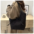 Minimalist black faux suede tote bag with a bow accent worn by a model in a warm room - Black