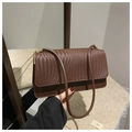 Detalle de bolso bandolera marrón oscuro con solapa trenzada y hebilla dorada - café