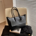 Minimalist black matte leather tote bag with unique handle lid design on a chair - Black