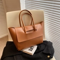 Caramel brown leather tote bag with wide handles and winged design on a white chair - Brown