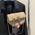 Beige saddle bag with litchi texture and gold studs on a black blazer backdrop - Khaki