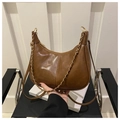 Detail of brown crescent shoulder bag with golden chain and zip closure on white books - Brown