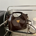 Dark brown patent leather tote bag with gold triangle logo in a modern urban setting - With Pendant / Brown